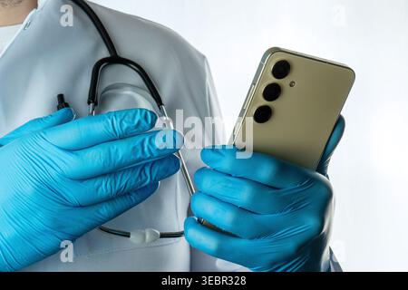 Doctor in blue medical gloves using smartphone, healthcare and telemedicine concept, close-up with stethoscope Stock Photo