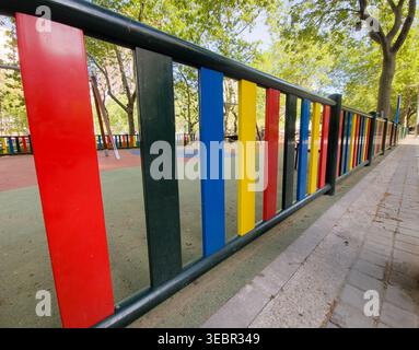 Brightly colored fence panels enclosing a vibrant playground area in an urban park Stock Photo