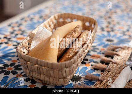 Assortment of fresh bread in a straw basket, served on a colorful Zellige tile table for a traditional Moroccan breakfast Stock Photo