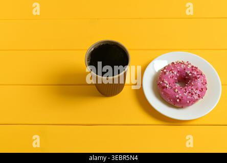 Coffee in a Brown Paper Cup and Pink Donut on Yellow Background Stock Photo