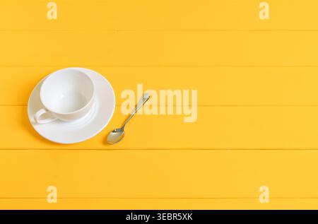 Empty White Cup with Saucer and Spoon on Yellow Wooden Background Stock Photo