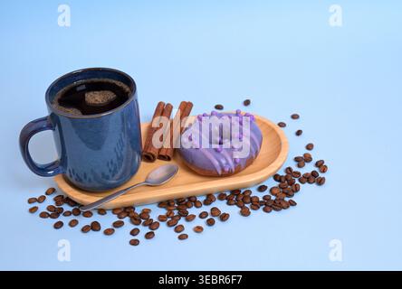 Black Coffee and Purple Donut with Cinnamon and Coffee Beans on Blue Background Stock Photo