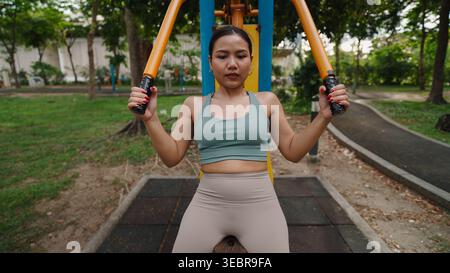 Concentrated sportswoman exercising on outdoor fitness equipment in a park, promoting healthy lifestyle and wellness Stock Photo