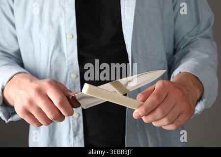 Man sharpening knife on grey background, closeup Stock Photo