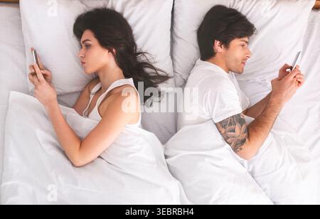 Couple Lying in Bed Using Smartphones, Disconnected in an Intimate Space Stock Photo