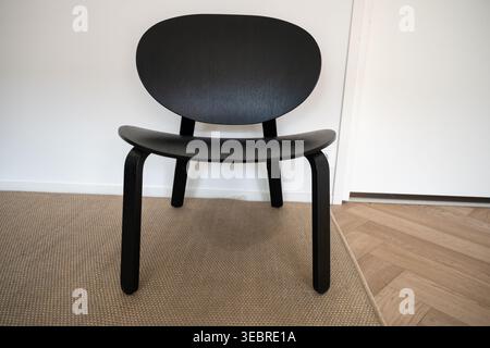 Modern black wooden chair in minimalist interior on carpet near white wall Stock Photo