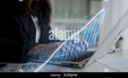 A businesswoman analyzes data on her laptop, with futuristic graphs displayed on the screen. This image captures a modern workspace focused on growth Stock Photo