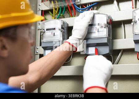 Electrician with screwdriver checking electrical meter indoors, closeup Stock Photo
