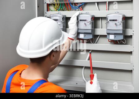 Electrician with screwdriver checking electrical meter indoors Stock Photo