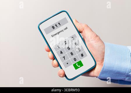 Hand holding smartphone displaying 911 emergency number and keypad on screen Stock Photo