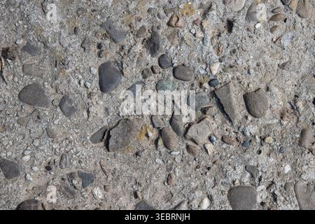 Rustic concrete texture with embedded river stones and pebbles, featuring a rough weathered surface ideal for construction, architectural, or organic Stock Photo