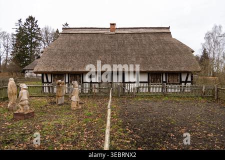 Kluki, Poland - January 06, 2023: Traditional architecture of an old village house with a thatched roof and wooden folk figures. Stock Photo