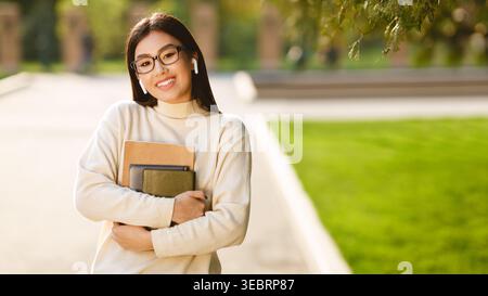 Student Smiling and Holding Books While Walking in a Sunny University Campus Stock Photo