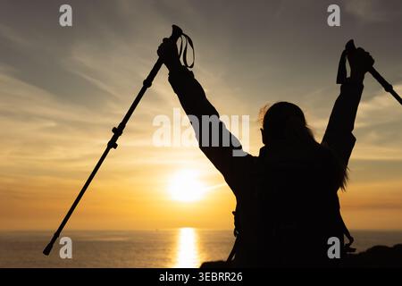 Woman feeling strong and achieving freedom, celebrating success on a coastal clifftop during a vibrant sunset, reaching a summit with a joyful express Stock Photo