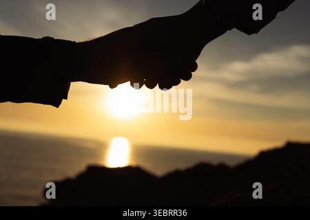 Two individuals shaking hands in silhouette at sunset, representing a successful partnership, agreement, cooperation, and the strong bond of teamwork Stock Photo