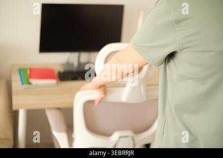 Woman adjusts new white ergonomic office chair in modern workspace. Person standing and make stretch exercise workout near home office desk. Stock Photo