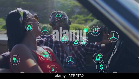 Taking selfie on hill, sunglassed plaid man, woman leaning in convertible with phone and eco icons Stock Photo