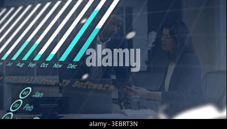 Collaborating pair in dark suits leaning over laptop in office with tablet, papers, chart overlay Stock Photo
