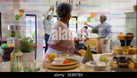 Holding bowl of popcorn, senior woman wearing pink cardigan greeting family in living room, buffet Stock Photo