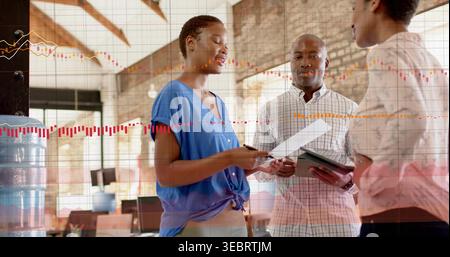 Examining papers, team wearing business shirts huddling in loft office, showing tablet with charts Stock Photo