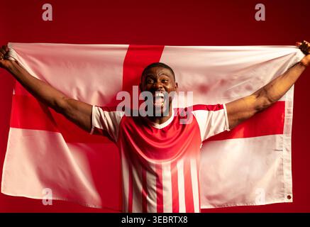Man in 30s holding white flag with red cross in studio, wearing red-and-white jersey, shouting Stock Photo