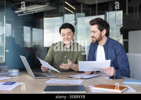 Two diverse businessmen collaborating, actively discussing paperwork, reviewing documents, and analyzing important data during a professional office m Stock Photo