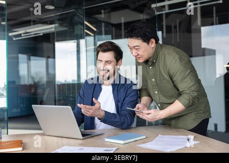Two diverse male colleagues collaborating on a laptop, discussing business ideas and sharing information, fostering teamwork and innovation in a conte Stock Photo