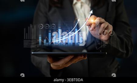 A business professional uses a tablet to analyze financial data while displaying graphs and growth indicators in a modern corporate environment. Scalp Stock Photo