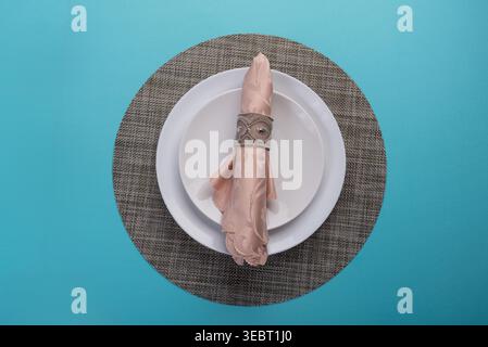 Overhead shot featuring delicate pink napkin on white plates. Neutral placemat on light blue backdrop. Soft, diffused lighting enhances textures. Suit Stock Photo
