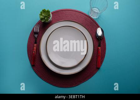 Overhead still life. Minimalist setup features white plates with golden rims, silverware, succulent, and glass. Shot in bright diffused studio light. Stock Photo