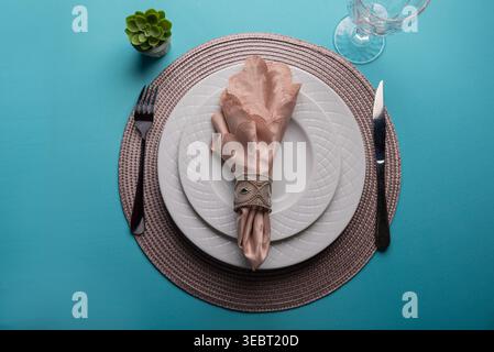 Overhead shot featuring minimalist table setting. Plates, cutlery, folded napkin. Clean tableware on turquoise. Gentle, diffused lighting. Perfect for Stock Photo