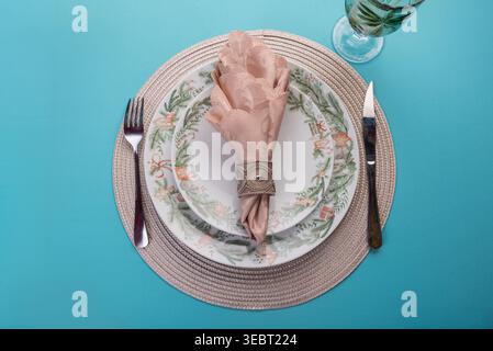 Overhead shot features Christmas themed table setting against a light blue backdrop. Includes decorative plates, napkin with ring, glass, fork and kni Stock Photo