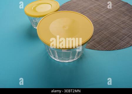 Studio shot with two glass bowls, each has a yellow lid; minimalist setup. Bowls show smooth glass texture; lids are solid. Harsh studio lighting, on Stock Photo