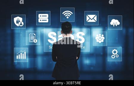 A business professional stands focused on the digital representation of Software as a Service, surrounded by various icons illustrating cloud-based Stock Photo