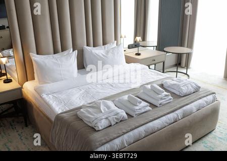 Hotel bedroom with towels and bathrobe placed on bed for guests. Hospitality preparation concept in modern rental interior. Stock Photo