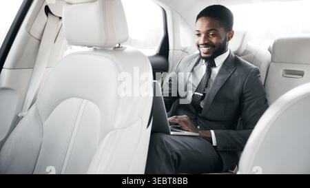 Business Professional Working on Laptop in Luxury Car While Commuting in Urban Area Stock Photo