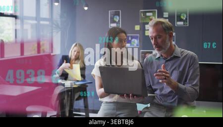 Working two colleagues wearing business attire reviewing laptop and charts in office, with papers Stock Photo