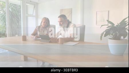 Reviewing documents, senior woman and mature man studying tablet at home dining wooden table, mugs Stock Photo