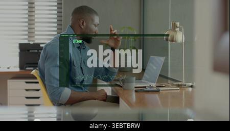 Analyzing man wearing blue shirt, sleeves rolled at office, viewing $120K overlay on laptop Stock Photo