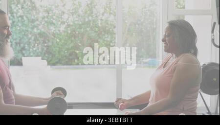 Lifting dumbbells, senior woman in pink tank and man in maroon top exercising on low bench Stock Photo