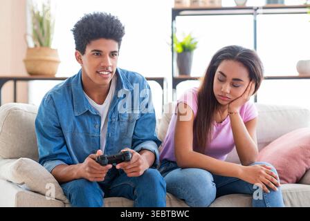 Two Young People Engage in Gaming Activity While One Appears Disinterested in the Experience Stock Photo