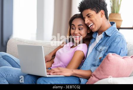 Young Couple Enjoying Time Together While Using a Laptop in a Cozy Living Room Stock Photo