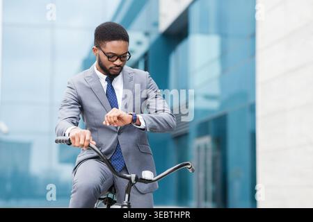 Businessman in Suit Checking Smartwatch While Riding Bicycle in Urban Setting Stock Photo