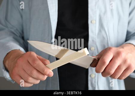 Man sharpening knife on grey background, closeup Stock Photo