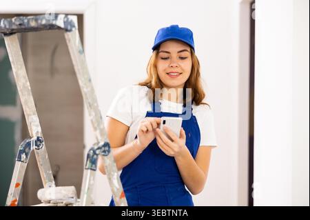 Positive young female contractor chatting online on smartphone Stock Photo