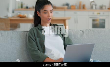 Happy smiling Arabian Indian woman use laptop celebrating win victory at home couch success excited champion freelancer student female working Stock Photo