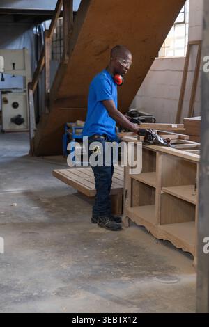 Woodworker using hand planer on wooden cabinet frame on sturdy workbench in carpentry workshop Stock Photo