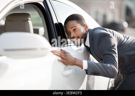 Excited Young Man Leaning on a White Car With a Joyful Expression Outdoors Stock Photo