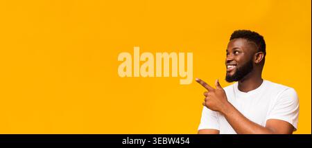 Engaging Young Man Smiling and Pointing Towards an Unseen Object Against a Bright Yellow Background Stock Photo