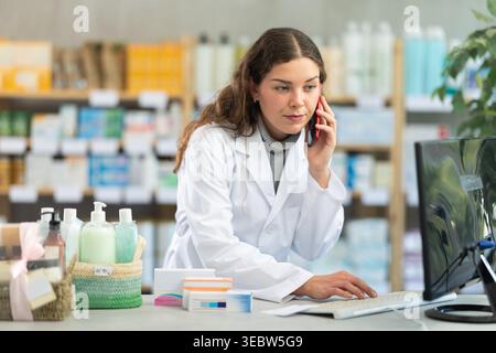Female pharmacist working at computer and talking on phone Stock Photo
